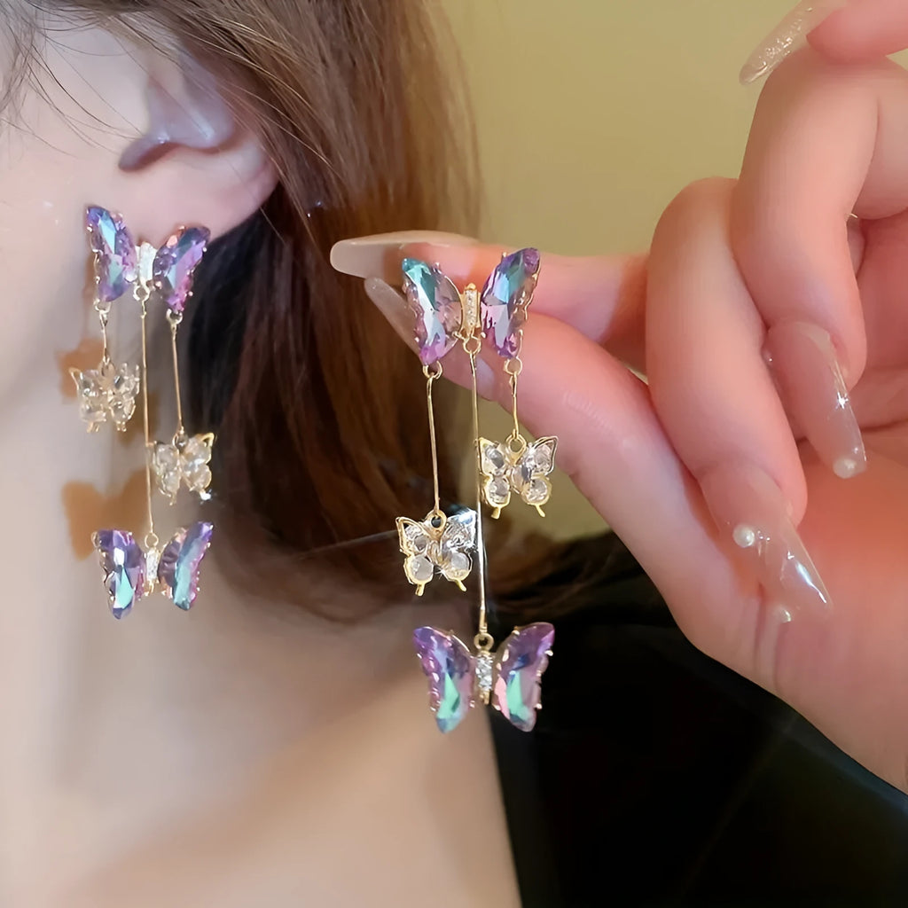 Silver toned earrings with a blue purple butterfly, crystal flowers, and a long tassel drop chain.