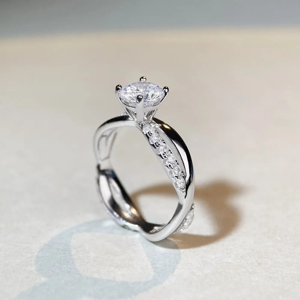 A geometric silver ring with a twisted band and a 1 carat moissanite stone in a four-claw setting.