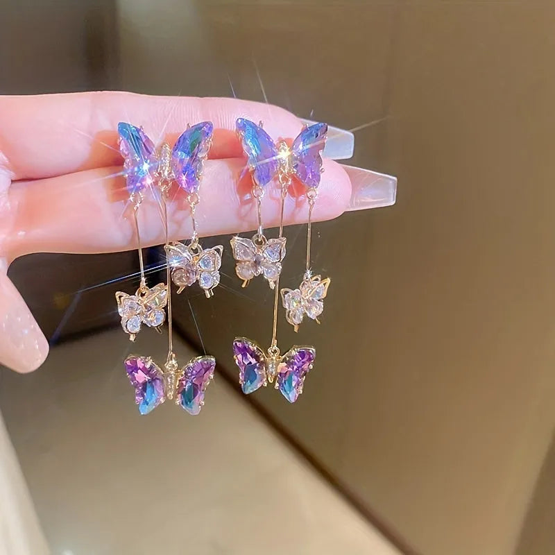 Silver toned earrings with a blue purple butterfly, crystal flowers, and a long tassel drop chain.