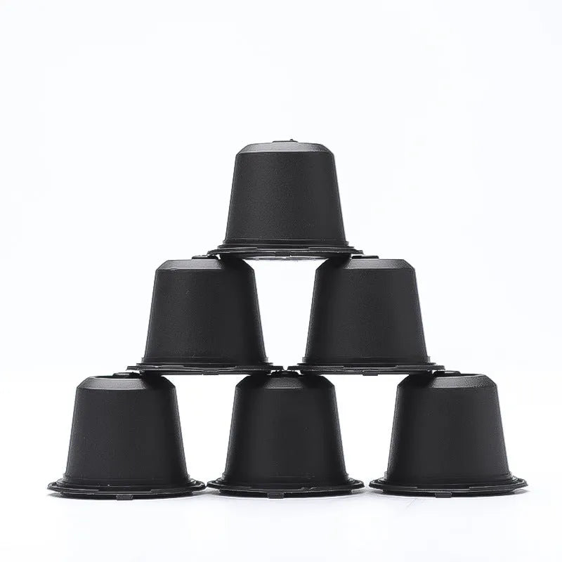 Six reusable black plastic coffee capsule filter cups with a spoon on a table