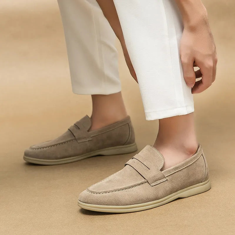 Men's brown leather slip-on casual shoes with round toe and rubber sole on a wooden floor.