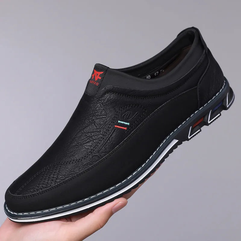 Men's black casual leather slip-on shoes with a rubber sole and visible sewing line details on a leather toe cap.