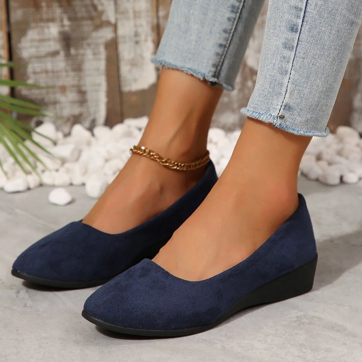 Women's black suede low wedge pumps with pointed toe and shallow mouth design on a rubber sole.
