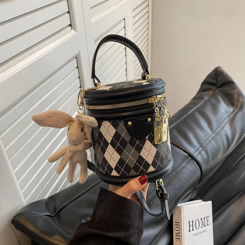 Textured rhombus cylindrical PU bucket bag in beige with white rabbit pendant, 14 cm wide.
