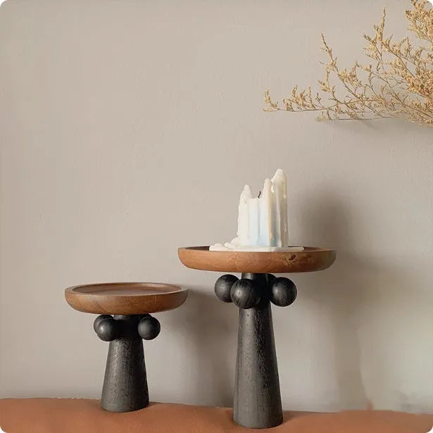 Round wooden tray with high Nordic-style legs in a light wood finish holding a candle