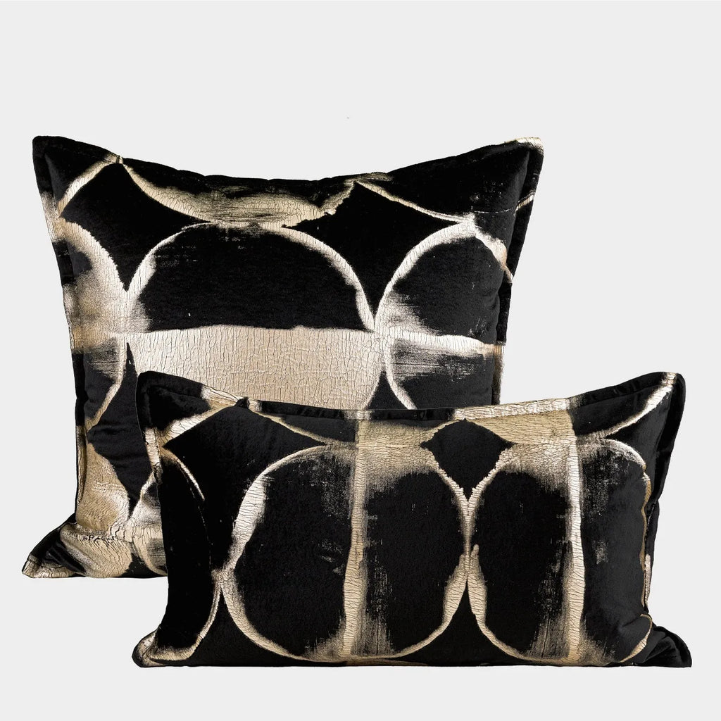 Black and gold abstract pattern decorative cushion with removable cover on a grey sofa.