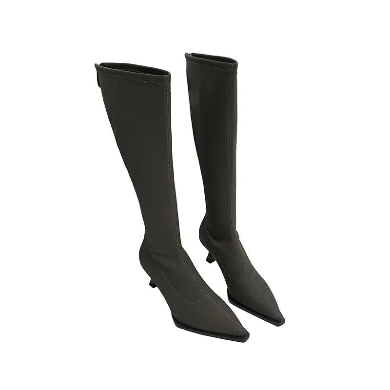 Black pointed toe knee-high boots with a stiletto heel and back zipper, shown on a model