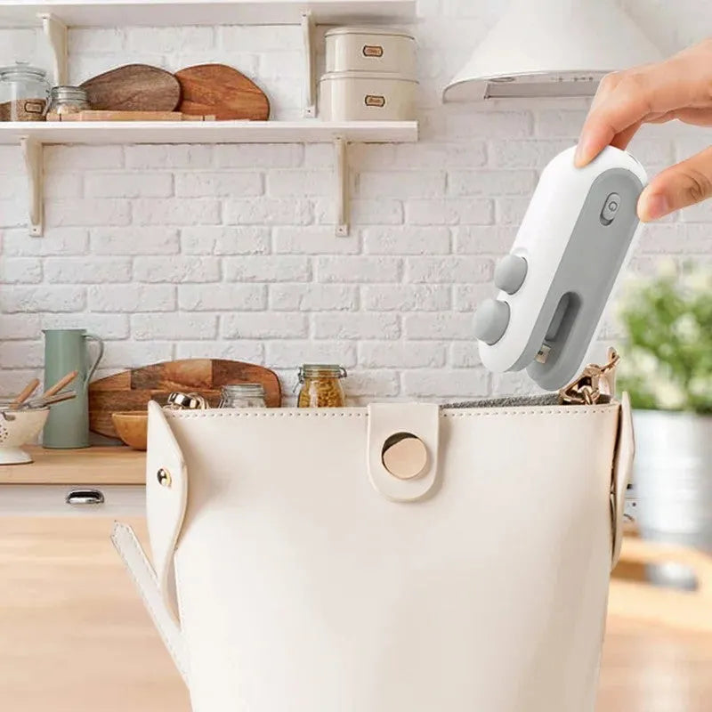 White handheld vacuum sealing machine with USB port and cutter blade on a kitchen counter.