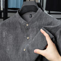 Man wearing a loose grey linen shirt with a stand collar and short sleeves, cardigan style.