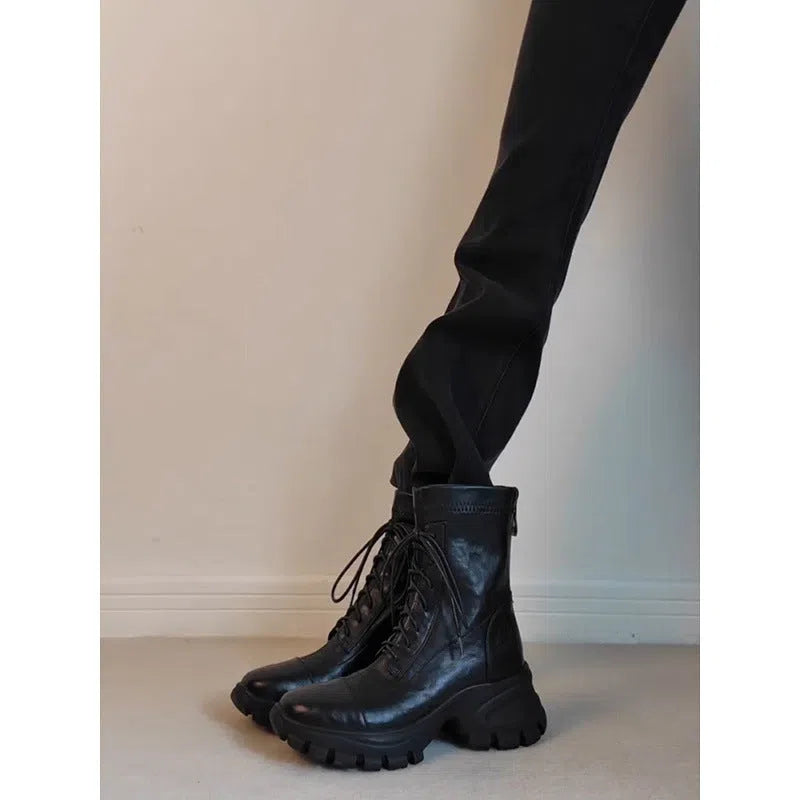 Black thick-soled motorcycle boots with back zipper and lace-up closure on a grey background