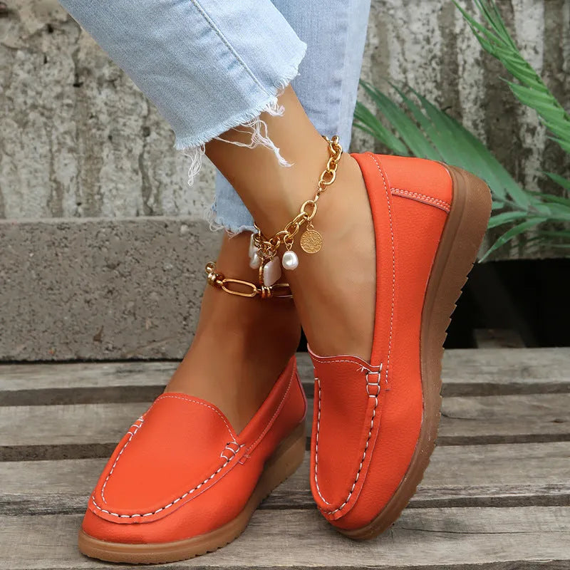 Women's flat slip-on loafers in PU leather with car stitch detail and a round toe, shown on a white background.