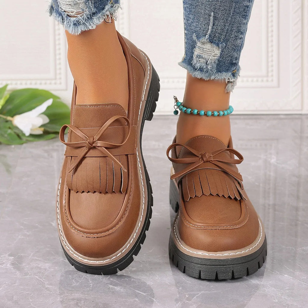 Black women's loafers with a tassel detail and chunky rubber sole on a wooden floor.