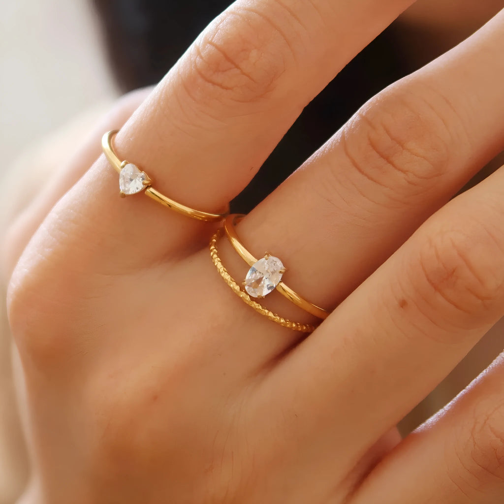 Golden electroplated stainless steel ring showing heart and oval shape designs on a hand.