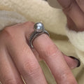 Adjustable open geometric copper ring with a black pearl for women on an index finger.