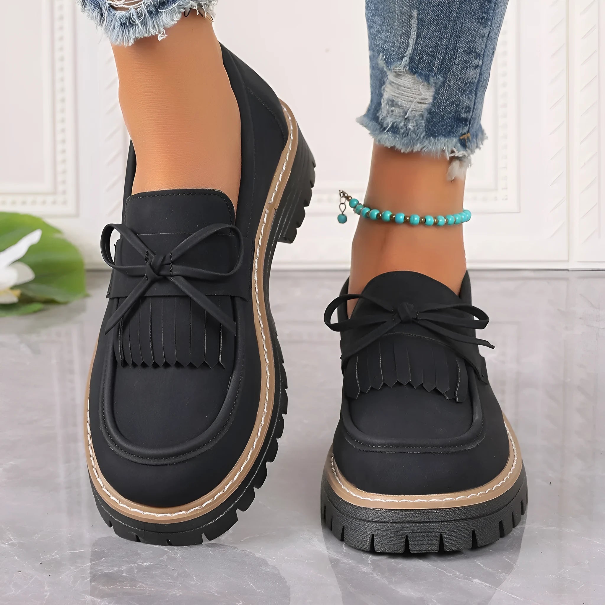 Black women's loafers with a tassel detail and chunky rubber sole on a wooden floor.