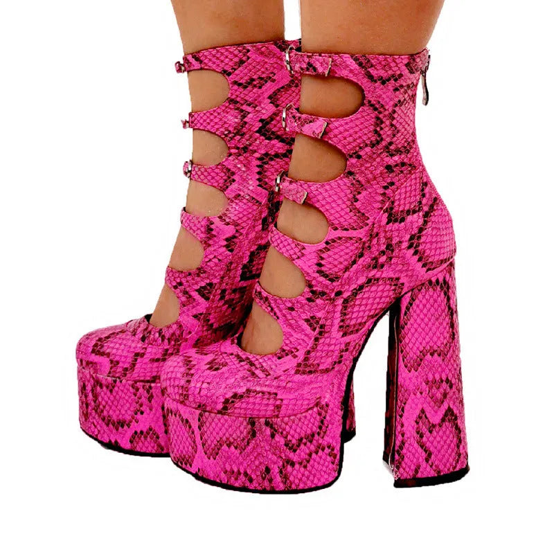 Women's black patent leather platform high heel boots with a serpentine belt buckle fastened around the ankle.