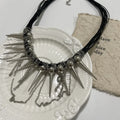 Close-up of a leather necklace with round beads, a winding tassel, and silver rivet details on a dark background.