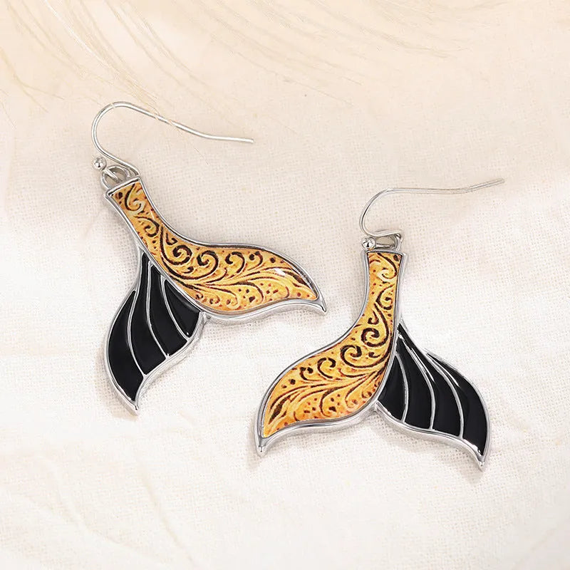 A pair of gold-coloured alloy fishtail earrings with a detailed whale tail design on post studs.