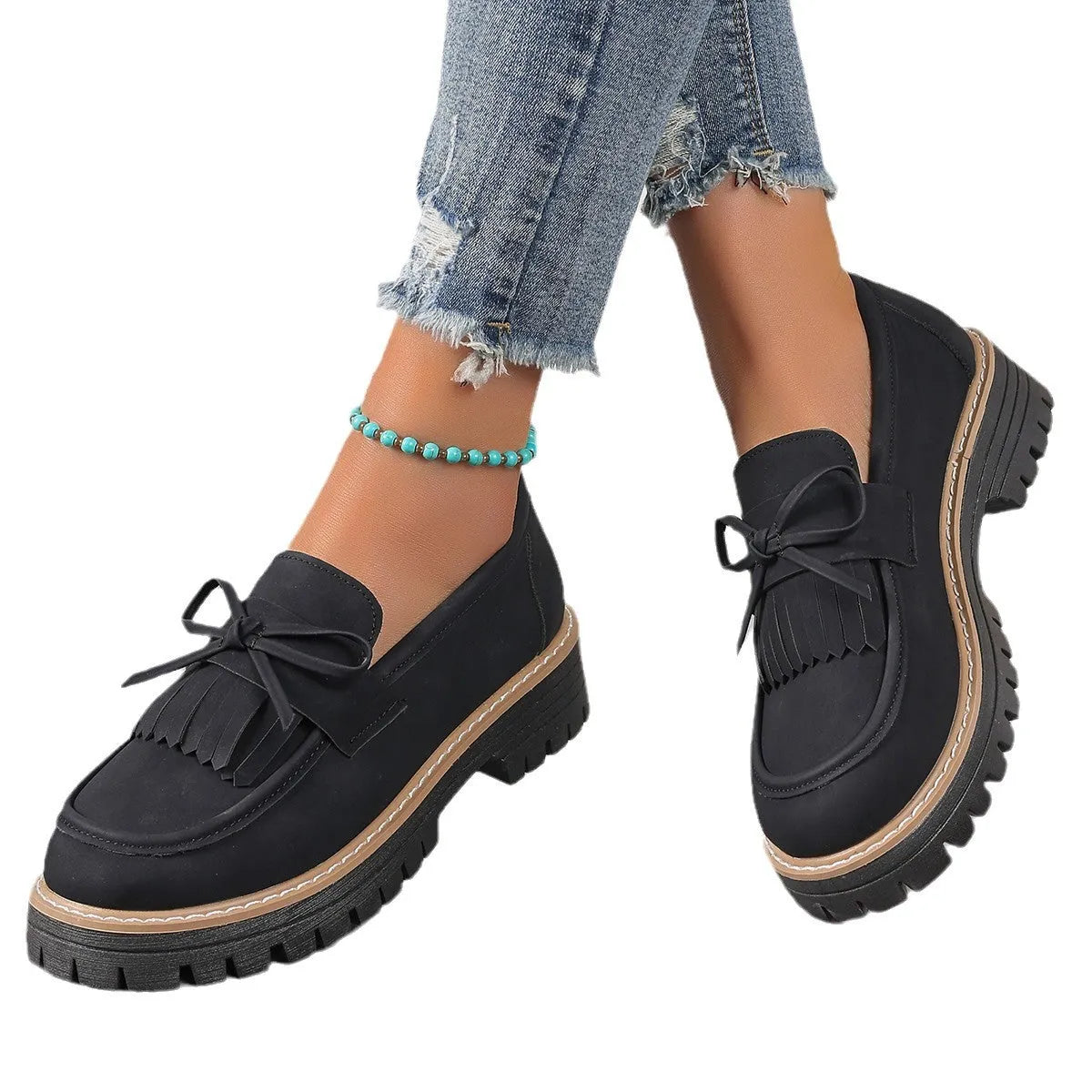 Black women's loafers with a tassel detail and chunky rubber sole on a wooden floor.