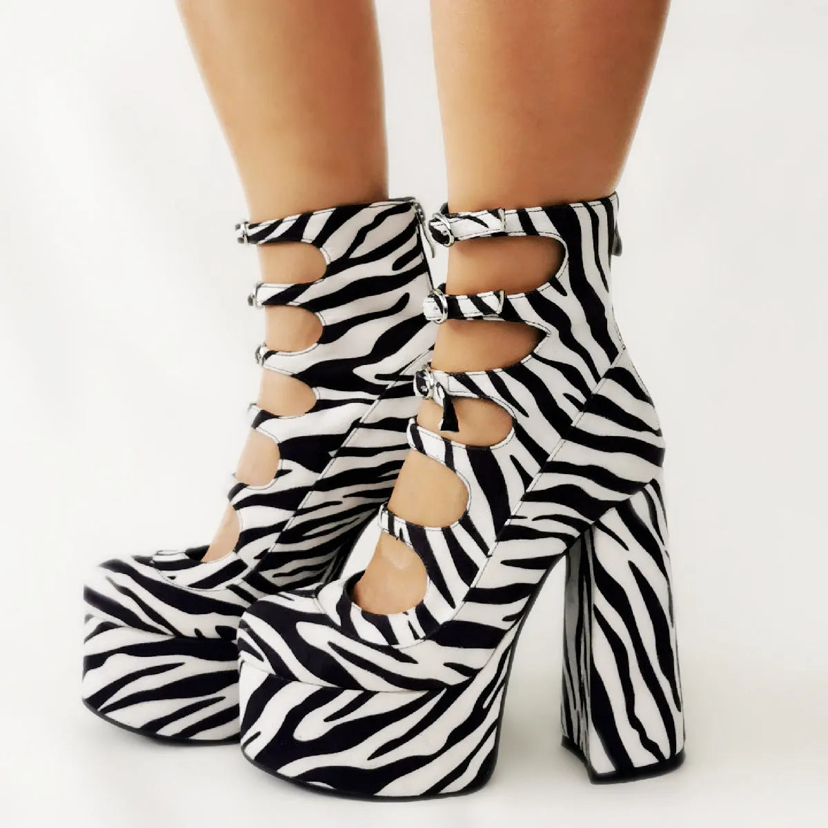 Women's black patent leather platform high heel boots with a serpentine belt buckle fastened around the ankle.