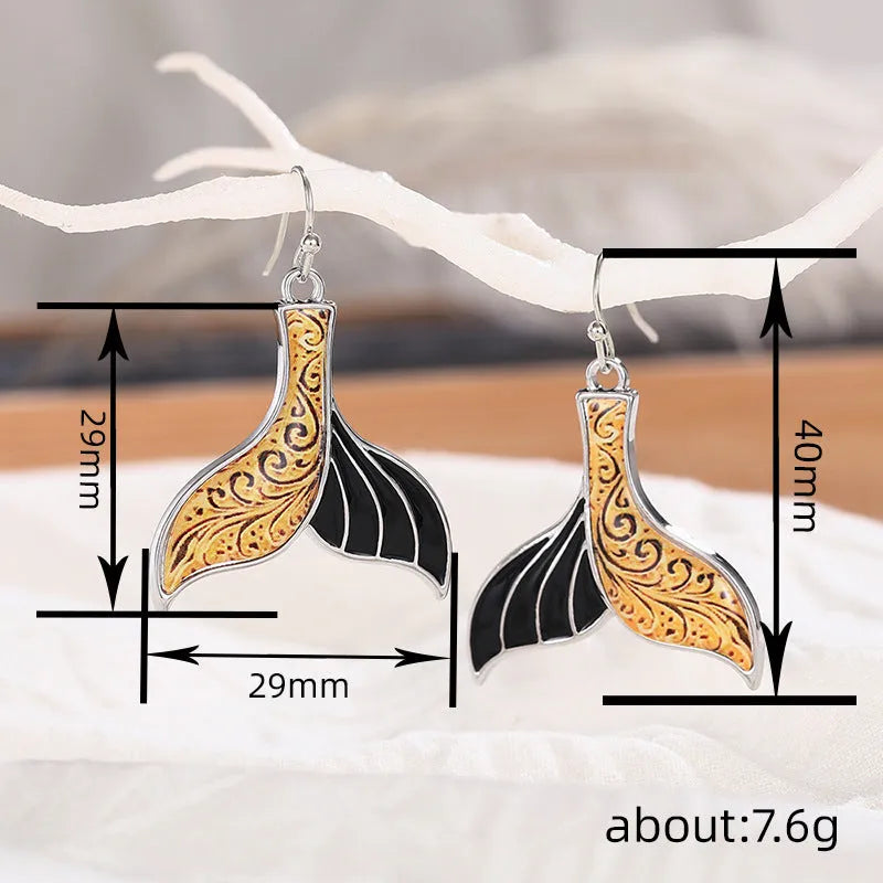 A pair of gold-coloured alloy fishtail earrings with a detailed whale tail design on post studs.