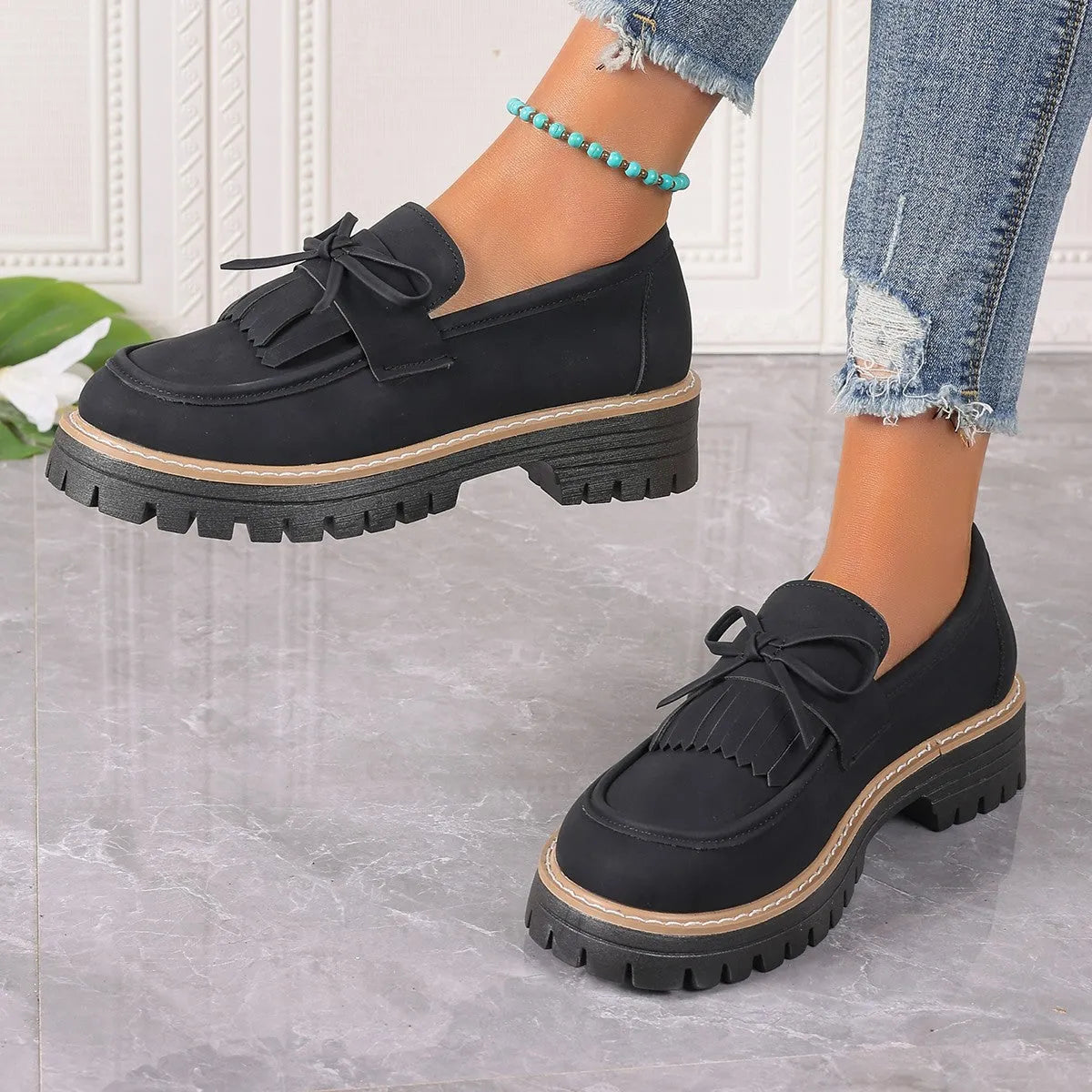 Black women's loafers with a tassel detail and chunky rubber sole on a wooden floor.