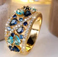 Women's hollow round fashion ring in gold or platinum finish with blue or white accents on a copper band.