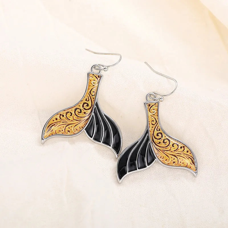 A pair of gold-coloured alloy fishtail earrings with a detailed whale tail design on post studs.