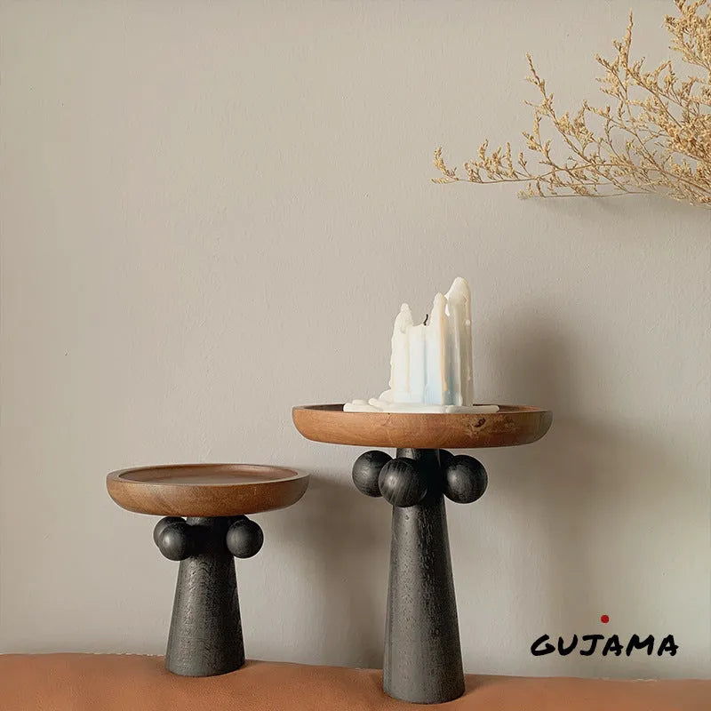 Round wooden tray with high Nordic-style legs in a light wood finish holding a candle