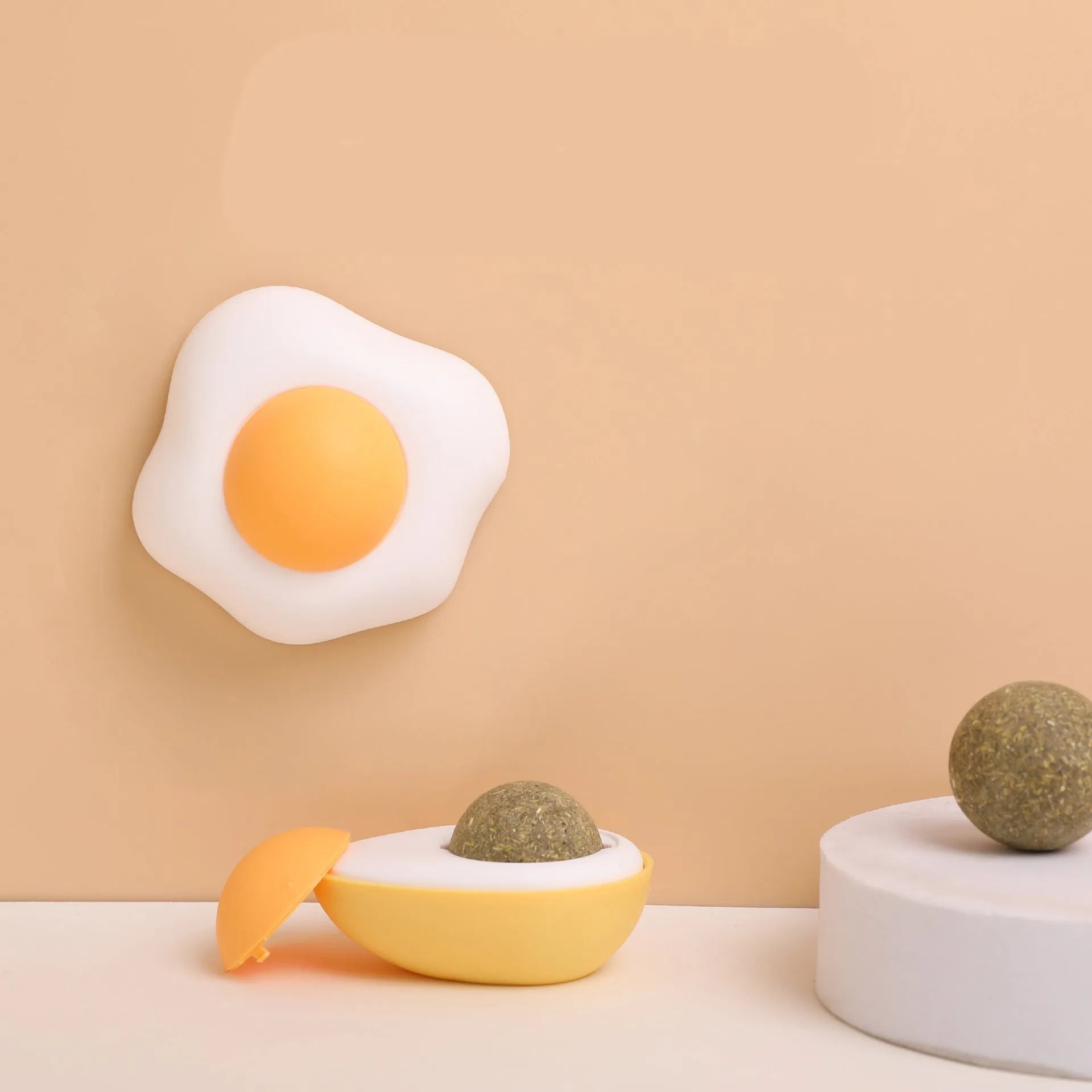Soft plush catnip ball toy in fried egg shape stuck to a wall, with a cat playing.