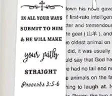 A polished stainless steel bookmark with an engraved inspirational verse, shown against an open book.