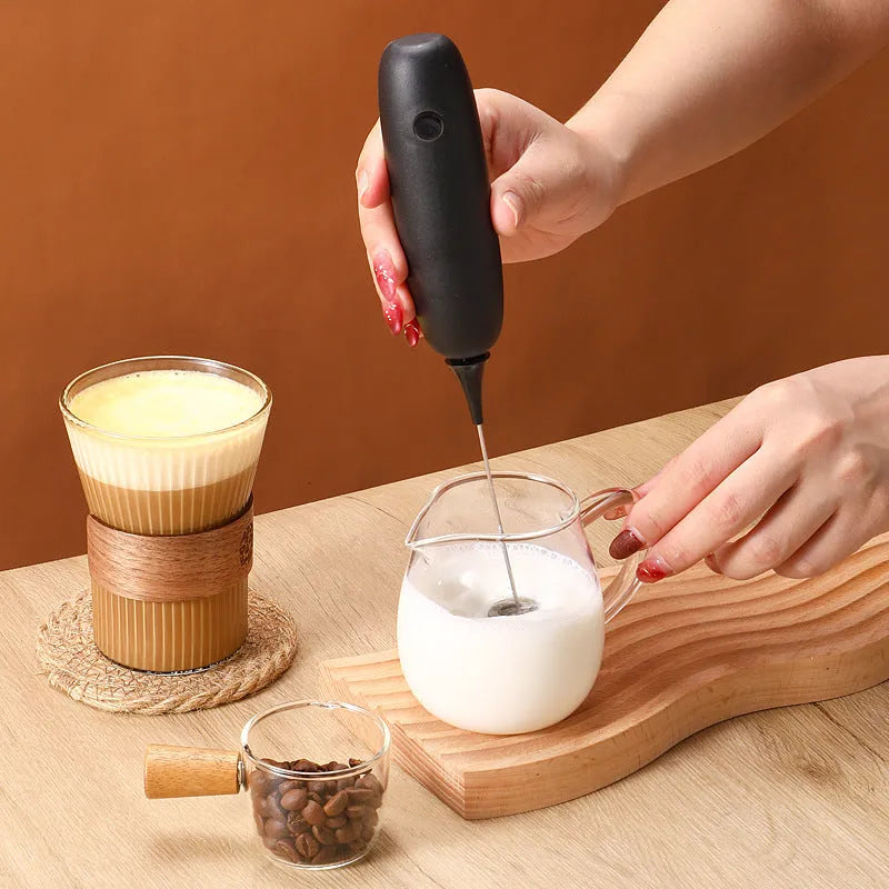 A hand-held electric milk frother in black and white colour options on a kitchen counter.