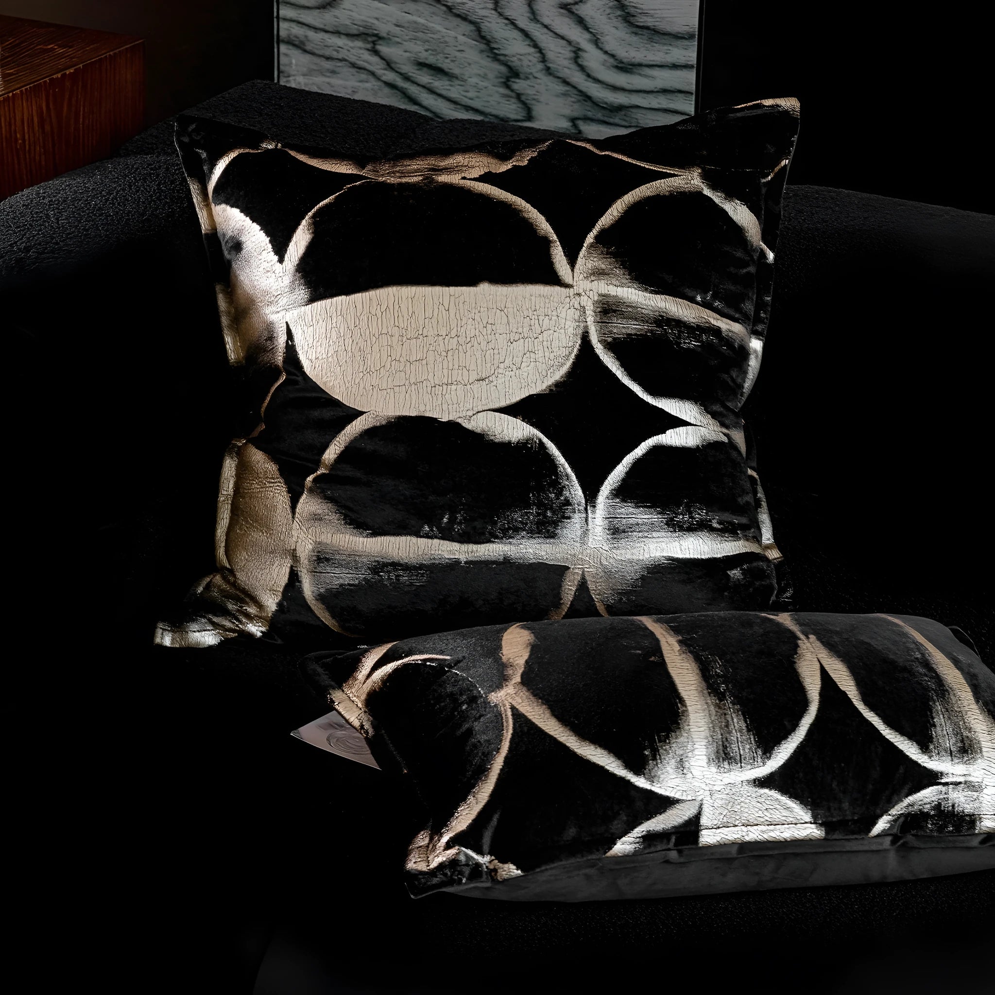 Black and gold abstract pattern decorative cushion with removable cover on a grey sofa.
