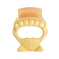 Green shell shaped plastic pet grooming comb with fine bent wire bristles on a white background.