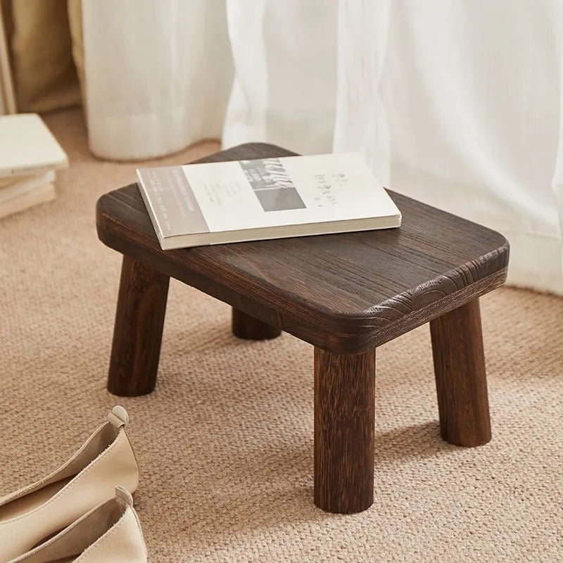 Solid wood distressed finish shoe changing stool with bracket legs in a living room setting.