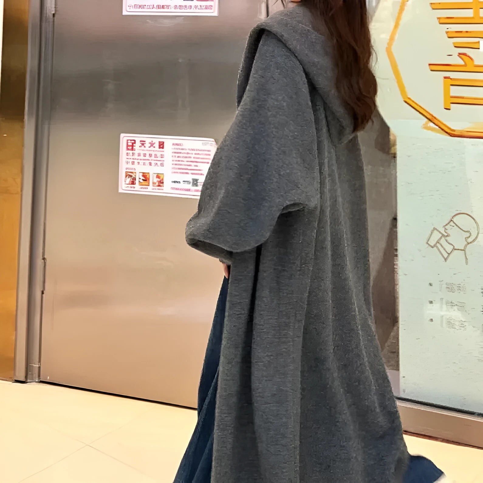 Long grey hooded knitted cardigan on a hanger showing its below-the-knee length and loose fit.