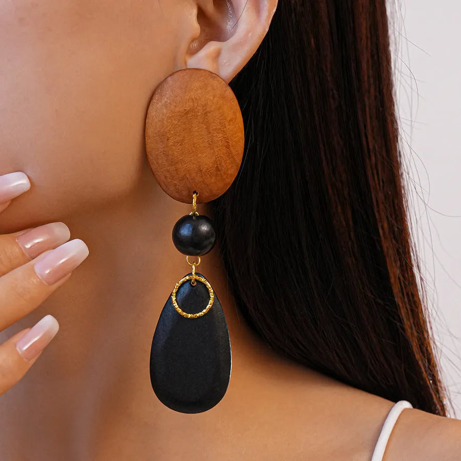 Handcrafted brown and black wooden elliptical earrings with silver needle detail on a retro style background.