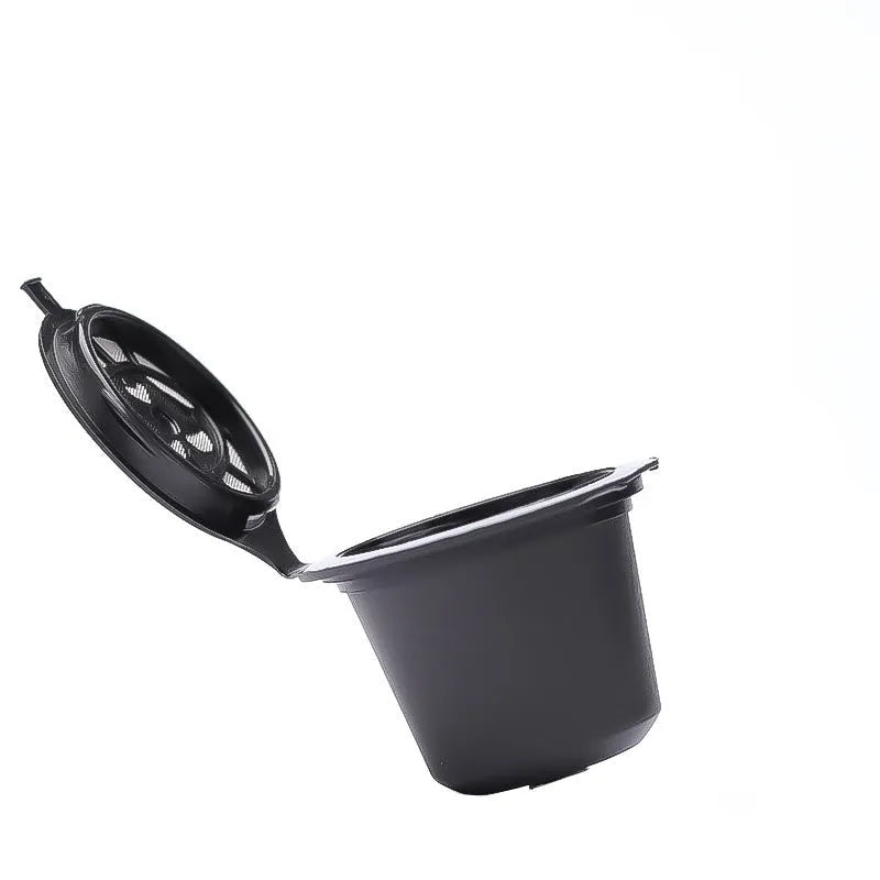 Six reusable black plastic coffee capsule filter cups with a spoon on a table