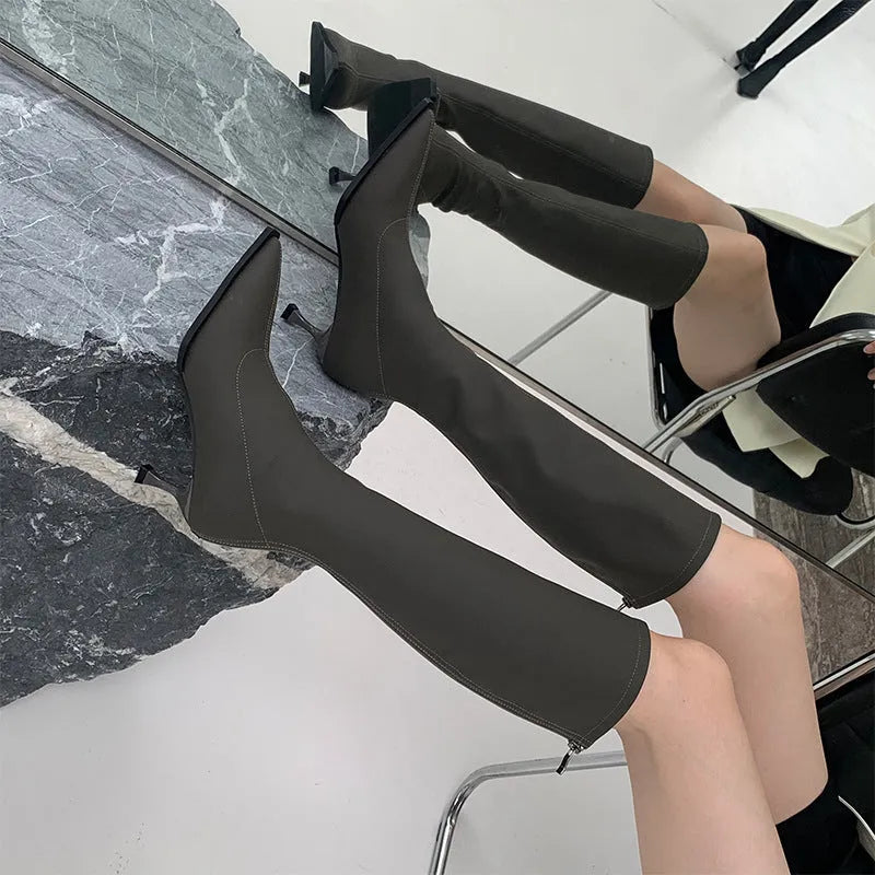Black pointed toe knee-high boots with a stiletto heel and back zipper, shown on a model