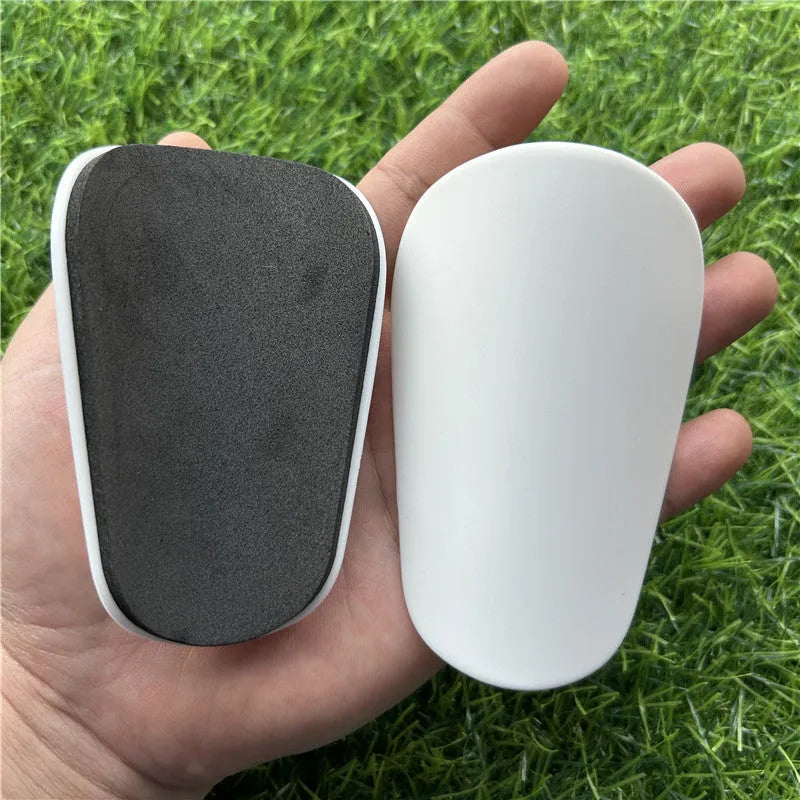 Pair of extra small black and white plastic football shin guards, size 8x5cm.