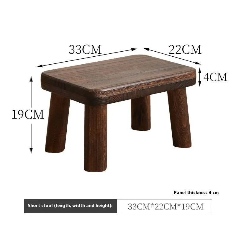 Solid wood distressed finish shoe changing stool with bracket legs in a living room setting.