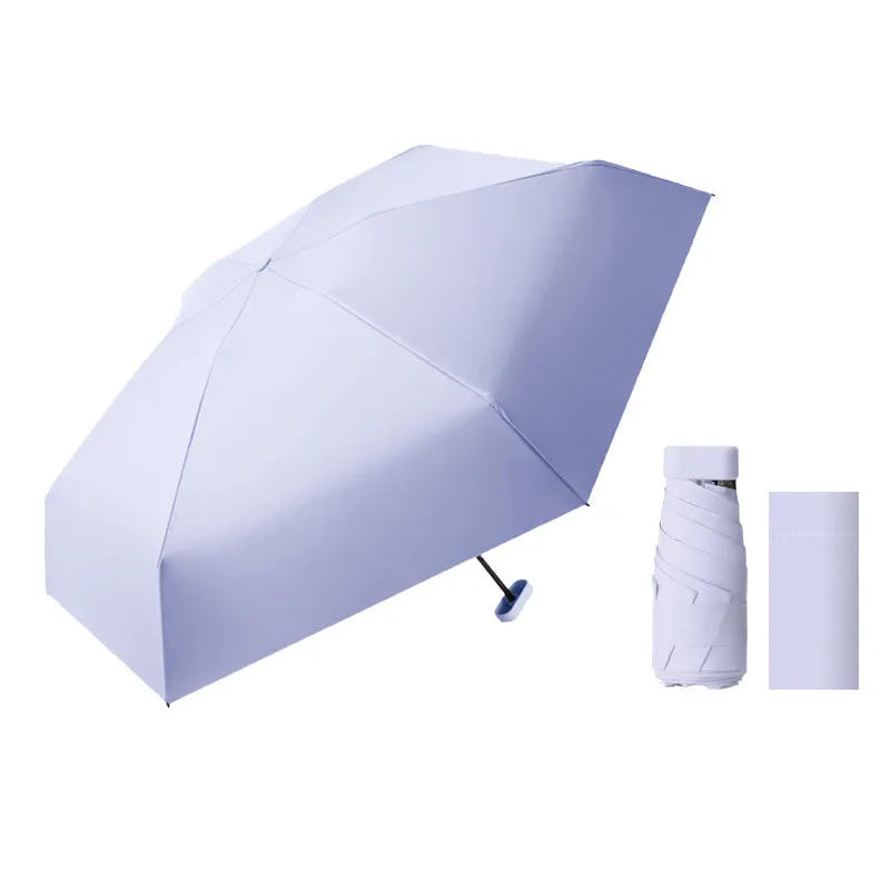 Ultra-light six-fold sun umbrella open, showing NC fabric canopy and rubber handle, next to its compact folded size in a capsule box.