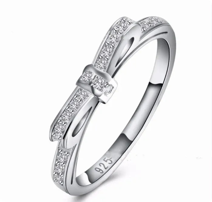 Silver-coloured bow-shaped ring with sparkling zircon crystal stones on a finger.