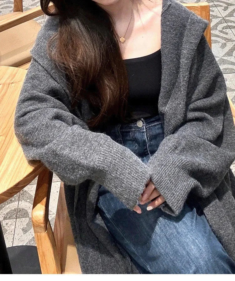Long grey hooded knitted cardigan on a hanger showing its below-the-knee length and loose fit.