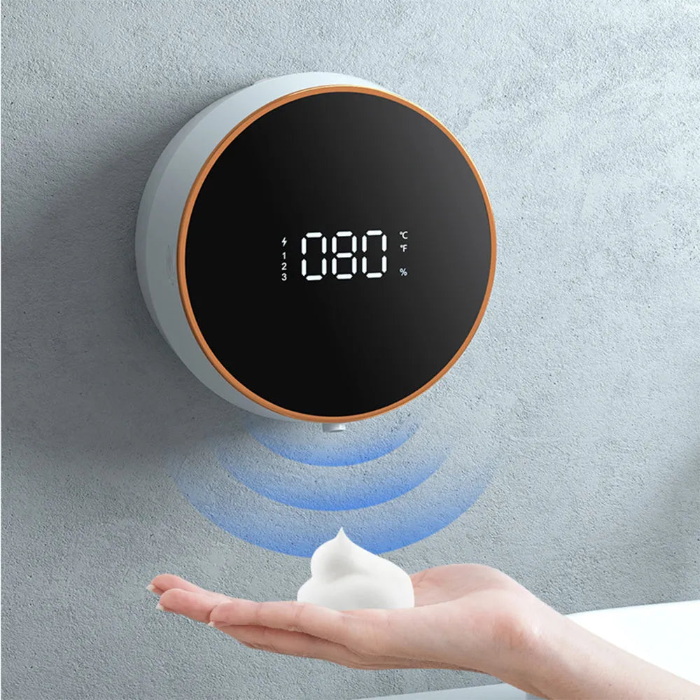 Black automatic sensor soap dispenser mounted on a white bathroom wall, dispensing foam.