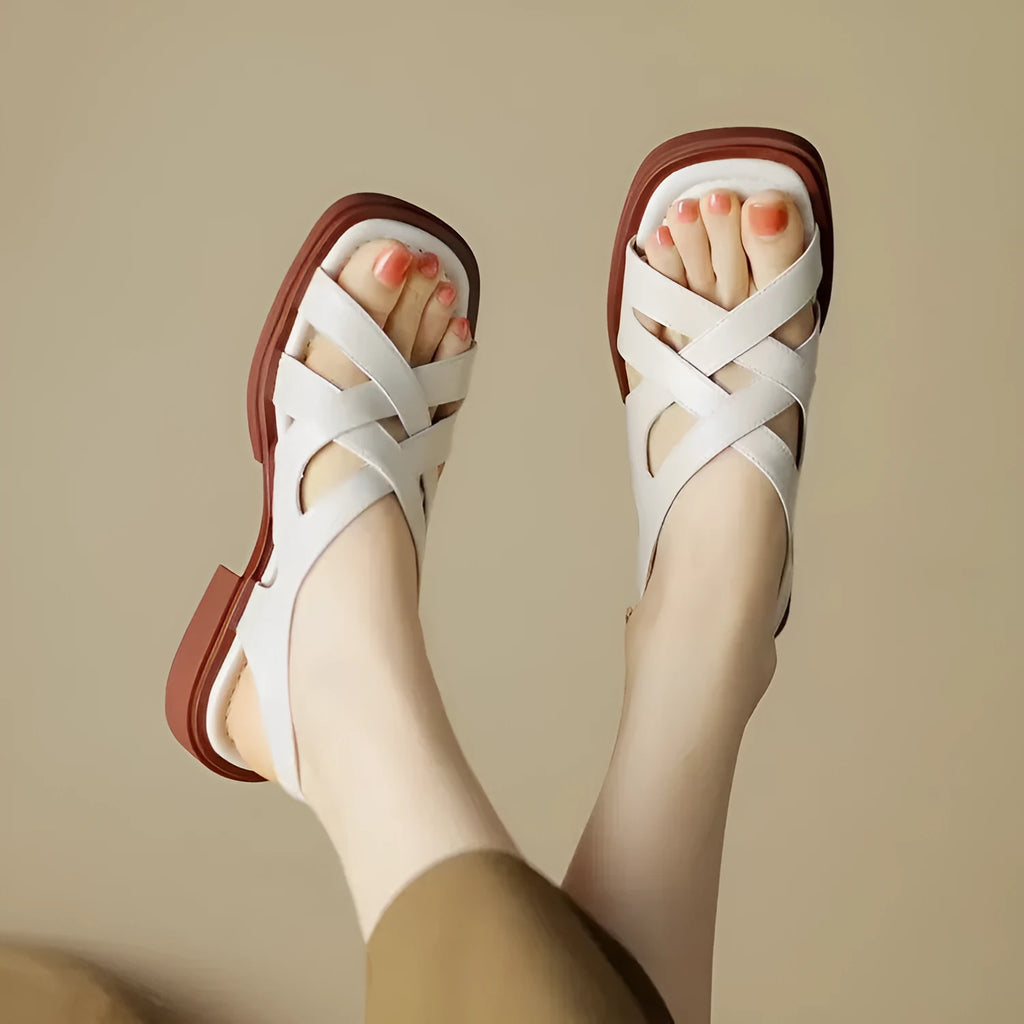 Women's glossy patent leather square toe sandals with cross strap on a brown background