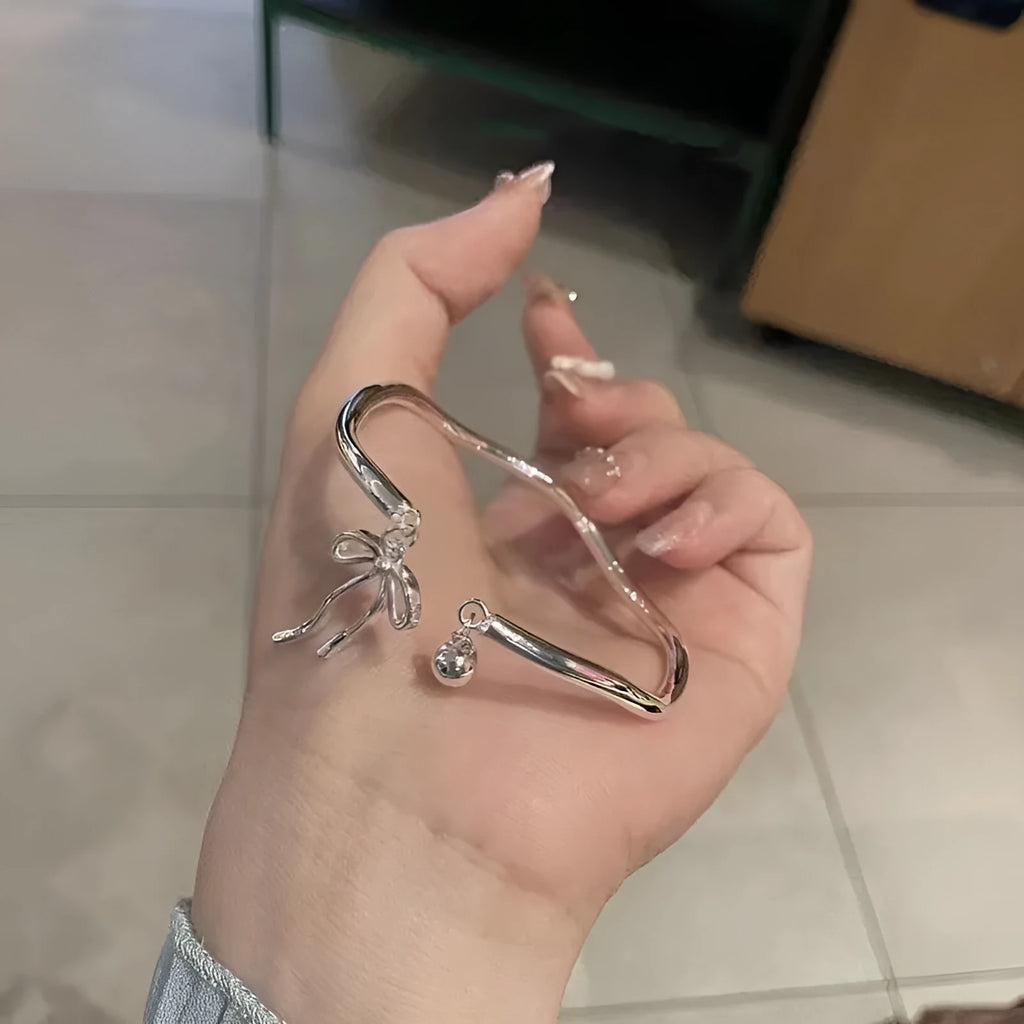 Silver adjustable bracelet with a detailed bow bell opening charm on a wrist.
