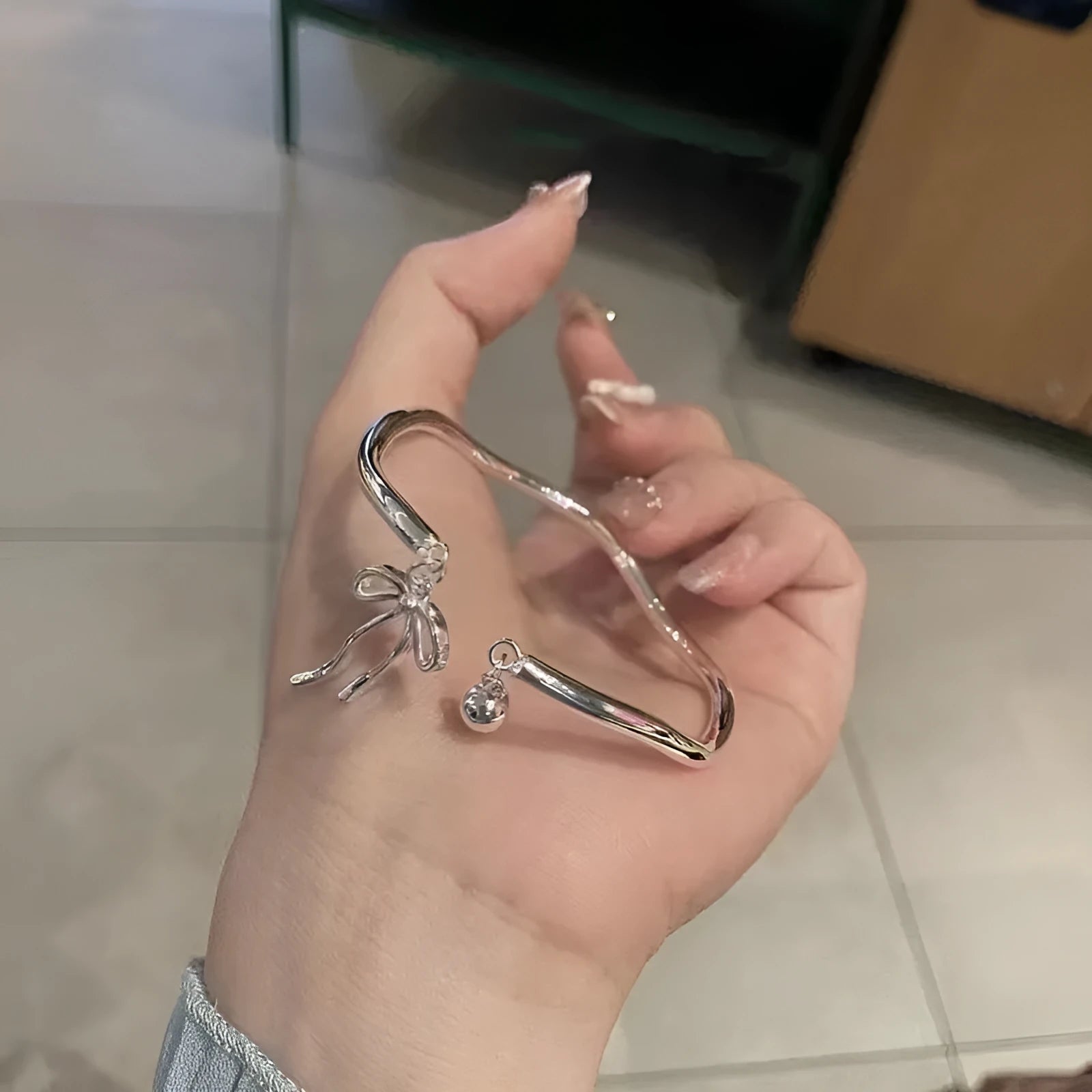 Silver adjustable bracelet with a detailed bow bell opening charm on a wrist.