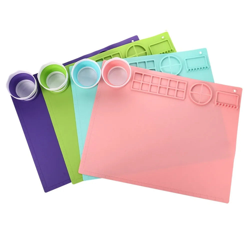 Light blue silicone painting mat with an integrated bowl on one side, positioned on a wooden table.