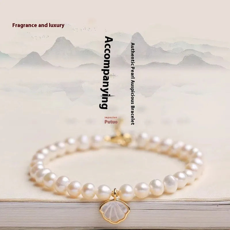 Women's freshwater pearl bracelet with central fan shell design on a wrist, showing elastic and chain fastening options.